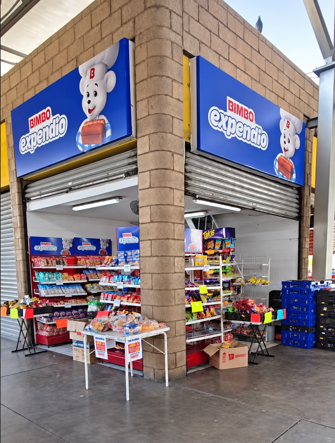 Entrada del Expendio de Pan Bimbo Central Milenium, con letreros azules y anaqueles de productos